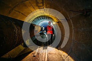Tunnel worker examines pipeline in underground tunnel photo
