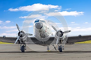 Turbo-prop vintage airplane parked at the airport, shiny metal fuselage aircraft against a background of clouds and a blue sky.