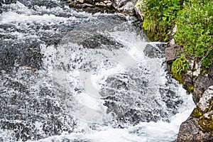 Turbulent spring stream of mountain river. Water foams, breaks into splashes on stones