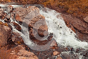 Turbulent spring stream of mountain river. Water foams, breaks into splashes on stones