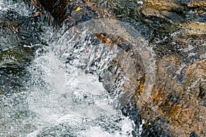 Turbulent spring stream of mountain river. Water foams, breaks into splashes on stones. Power of nature