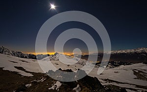 Turin city lights, night view from snow covered Alps by moonlight. Moon and Orion constellation, clear sky, fisheye lens. Italy.