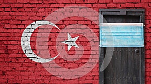 Turkey flag painted on brick wall and closed door with medical mask protected