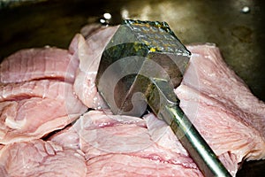 Turkey meat cut into pieces and a hammer for beating the meat. Close-up, surface texture