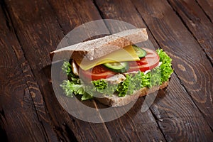Turkey sandwich closeup with fresh tomatoes, lettuce salad leaves, cucumber and cheese, on wooden rustic table background