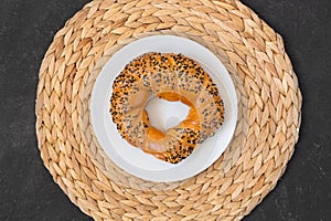 Turkish bagel simit with sesames on white plate and wicker napkin on black background. Top view