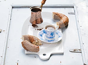 Turkish black coffee served in traditional ceramic cup with pattern, sesame bagel called simit on white serving board