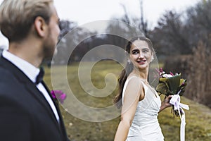 Turkish bride with beautiful smile on her face leading her newlywed husband. Outdoor late autumn photoshoot. Marriage