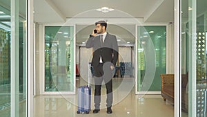 Turkish business man person with suitcase luggage walking to hall corridor and using mobile smartphone in a hotel in business trip