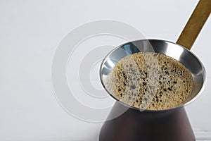 Turkish coffee pot with hot drink on white wooden table, closeup. Space for text