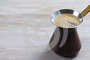 Turkish coffee pot with hot drink on white wooden table, space for text