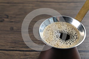 Turkish coffee pot with hot drink on wooden table, closeup. Space for text