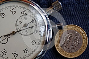 Turkish coin with a denomination of 1 lira and stopwatch on dark worn blue denim backdrop - business background