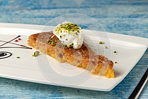 Turkish dessert ekmek kadayifi with milk cream and pistachio on a white porcelain plate