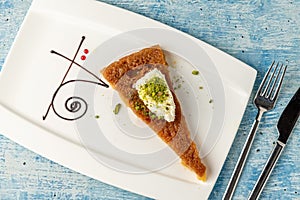 Turkish dessert ekmek kadayifi with milk cream and pistachio on a white porcelain plate