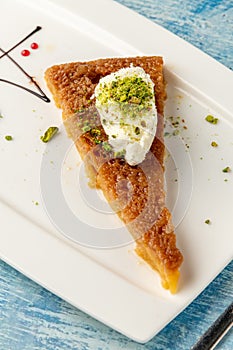 Turkish dessert ekmek kadayifi with milk cream and pistachio on a white porcelain plate