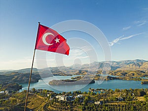 Turkish flag fluttering above picturesque Green Lake Manavgat. Lush green mountainous landscape with clear blue waer