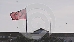 Turkish flag swaying in the wind against a clear blue sky. Action. Red flag of Turkey waving above the building and