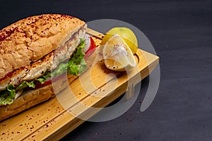 Turkish food sandwich balik Ekmek with grilled mackerel, tomatoes, onions and lettuce served with lemon closeup on the table.