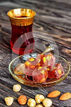 Turkish joys with different nuts is a glass of tea and a spoon. Eastern sweets. Traditional Turkish delight Rahat lokum on a