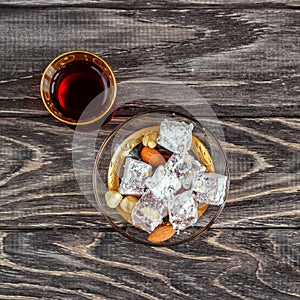 Turkish joys with different nuts is a glass of tea and a spoon. Eastern sweets. Traditional Turkish delight Rahat lokum on a