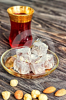 Turkish joys with different nuts is a glass of tea and a spoon. Eastern sweets. Traditional Turkish delight Rahat lokum on a