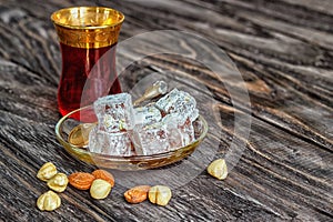 Turkish joys with different nuts is a glass of tea and a spoon. Eastern sweets. Traditional Turkish delight Rahat lokum on a