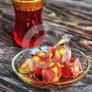 Turkish joys with different nuts is a glass of tea and a spoon. Eastern sweets. Traditional Turkish delight Rahat lokum on a