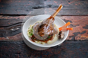 Turkish lamb shank in dark sauce with potato puree and vegetables on rustic wooden table