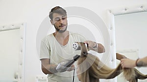 Turkish man hairdresser stylist dries long female hair drier.