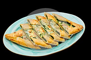 Turkish pizza pide with spinach and cheese lies on a plate on a black isolated background