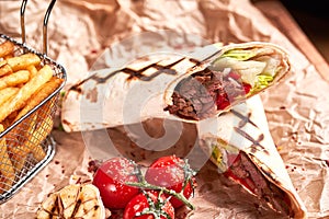 Turkish Shawarma with beef and fried with tomatoes on craft paper on wooden plate. Fast food set. Closeup view