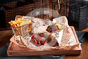 Turkish Shawarma with beef and fried with tomatoes on craft paper on wooden plate. Fast food set. Side view