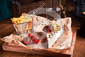 Turkish Shawarma with beef and fried with tomatoes on craft paper on wooden plate. Fast food set. Side view