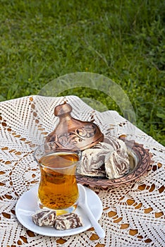 Turkish tea in a glass Cup and marble halva on a table with a handmade tablecloth and candy maker on a Sunny day