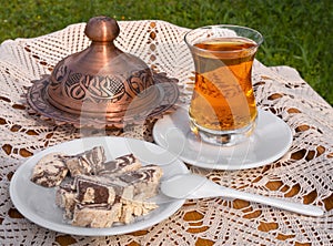 Turkish tea in a glass Cup and marble halva on a table with a handmade tablecloth and candy  maker on a Sunny day