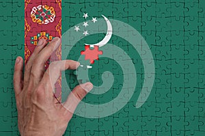 Turkmenistan flag is depicted on a puzzle, which the man`s hand completes to fold