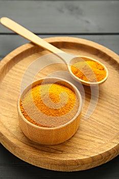 Turmeric (Curcuma) powder on wooden plate on black background