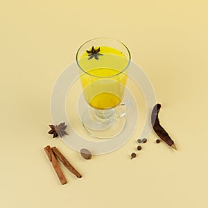 Turmeric latte with cinnamon sticks and anise herb on light-yellow background. Immunity boosters concept. Alternative