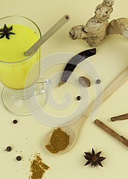 Turmeric latte with cinnamon sticks and anise herb on light-yellow background. Immunity boosters concept. Alternative