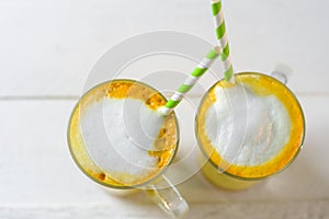 Turmeric latte or golden milk in glasses with green straw on a white table