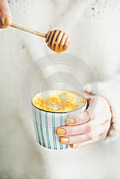 Turmeric latte, golden milk with honey in woman`s hands, close-up