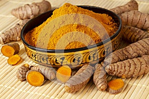 Turmeric powder in asian bowl with fresh turmeric roots selective focus on turmeric powder