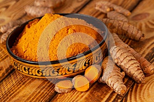 Turmeric powder in a asian bowl and turmeric roots in close up