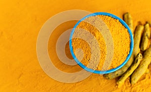 Turmeric powder in blue bowl with dry roots at orange background