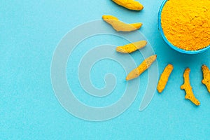 Turmeric powder in blue bowl and dry roots in shape of sun at blue background