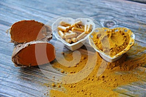 Turmeric powder, fresh organic turmeric and turmeric pills in a heart-shaped bowl on a wooden table, top view.