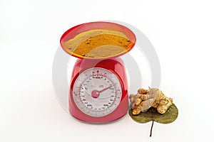 Turmeric powder and fresh turmeric root in red weight scale on