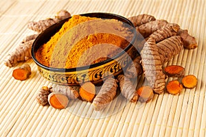 Turmeric powder and roots in asian bowl on bamboo napkin