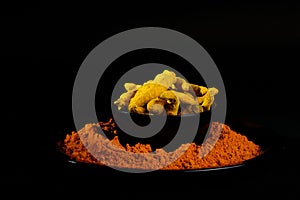 Turmeric powder and roots or barks on black background